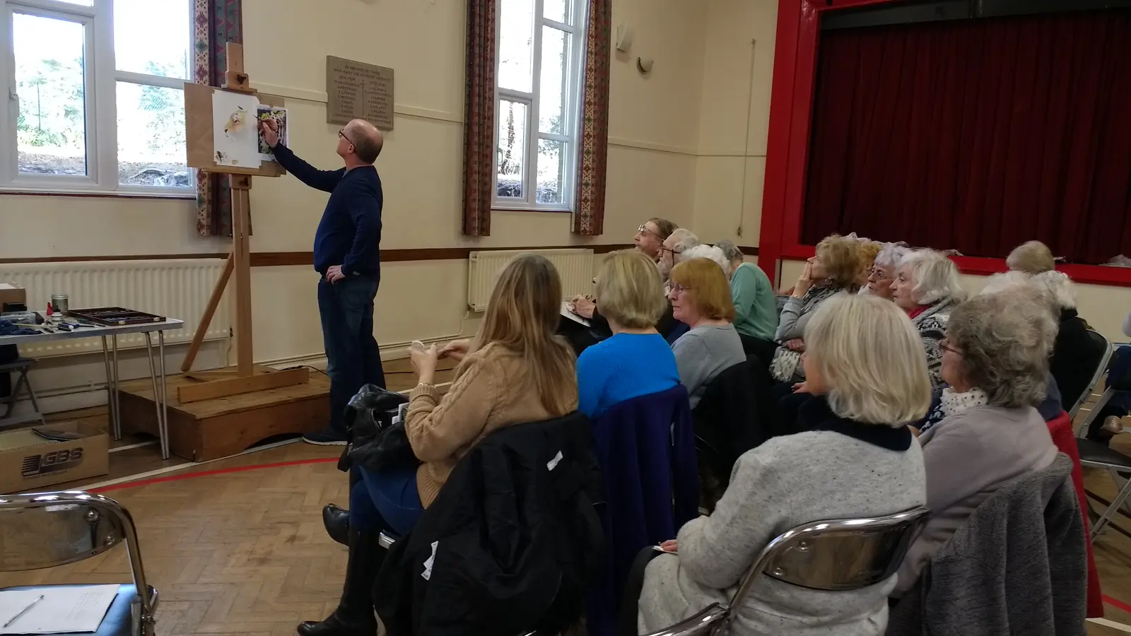 A visiting artist demonstrating at an easel to seated members