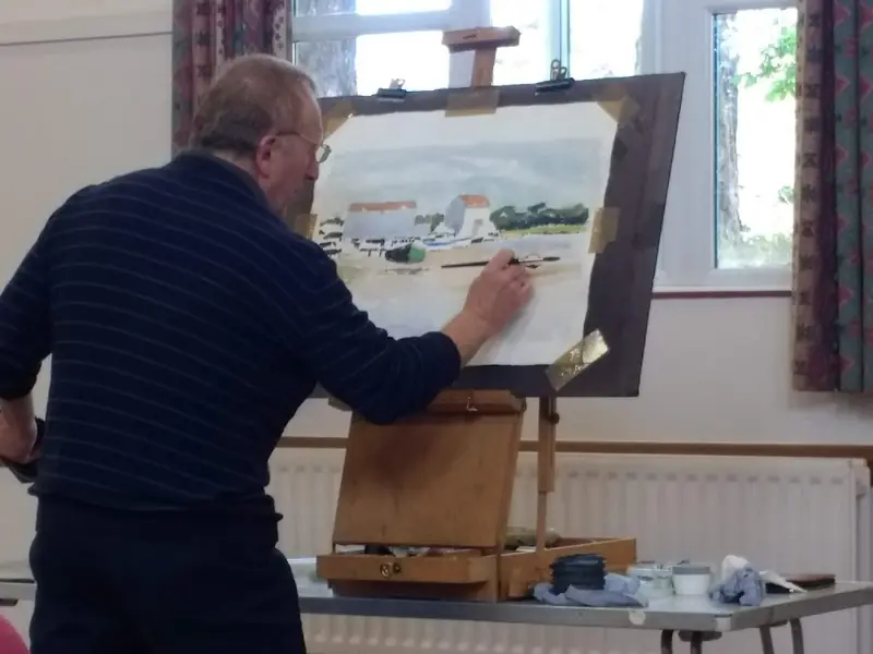 A member painting a harbour scene at an easel
